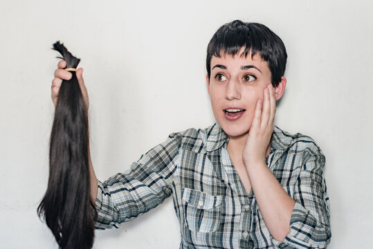 Mujer joven con pelo corto sosteniendo su cabello cortado en una cola de caballo. Concepto de donaci&oacute;n de cabello para pacientes con c&aacute;ncer.