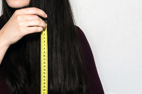 Detalle de una mujer morena sosteniendo una cinta m&eacute;trica amarilla para medir la longitud de su cabello largo y negro