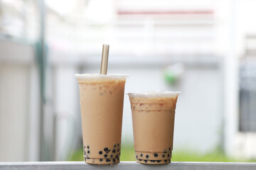Two cup big and small iced milk tea wih bubble boba fresh and sweet drink Taiwan style put on the steel bar and blur background , food and drink concept - obrazy, fototapety, plakaty