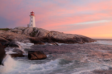 Peggy’s Cove Lighthouse illuminated at sunset with dramatic waves on the foreground, Nova Scotia,...