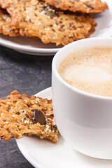 Cup of white coffee and fresh baked oatmeal cookies with honey and healthy seeds on plate. Delicious crunchy dessert