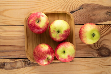 Several ripe apples on a bamboo plate on a wooden table, top view.