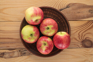 Several ripe apples in a ceramic plate on a wooden table, top view.