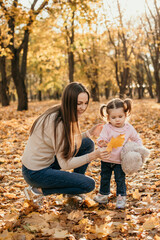Happy family mom and toddler baby girl playing outdoors in fall park. Little girl and her mother in...