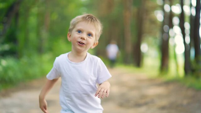 Close up portrait young happy cheerful kid. child running through woods. little boy having fun run. look camera on alley park forest. Happiness preschool blond blue eyes smiling toddler coming forward