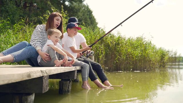 young happy family with little boy fishing a camping site. Parents with kids fishing together sitting on a wooden pier by pond spending weekend holiday outdoors. catching the fish, spend leisure time
