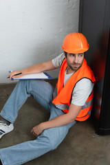 Young workman with clipboard sitting on floor