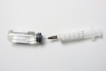 Vaccine vial and syringe on white on light grey background.