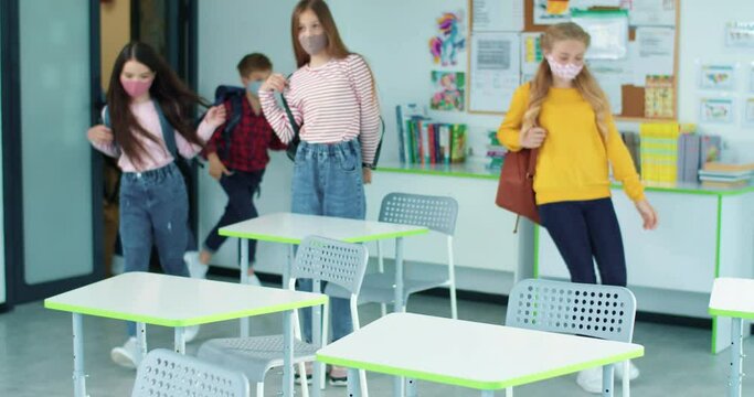 Many Caucasian children pupils in masks entering classroom with backpacks after coronavirus quarantine lockdown. Elementary school reopening, classmates at class, studying, education concept