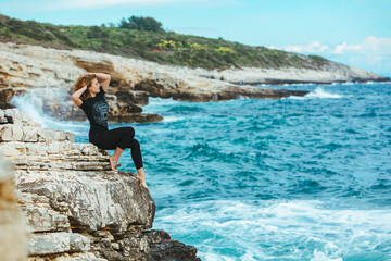 Obraz premium young slim woman sitting on the cliff edge looking at sea