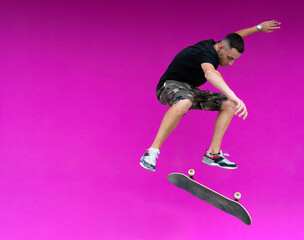 View of man jumping with skateboard on pink background.	