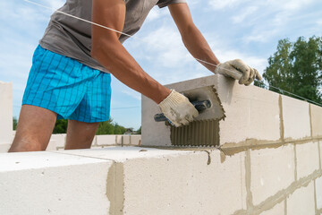 Builder uses a notched trowel to apply the cement mixture to the side of the building block. Concept of building houses