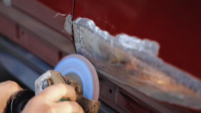 Close-up Of Worker Grinds Car Damage. Hard Grinding Is Designed To Smooth Out Irregularities. Professional Auto Workshop Worker Grinds Dented Door Of Car