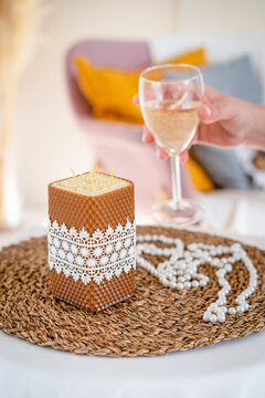 Handmade wax candle with white lace ribbon. Romantic setting. Hand with a glass of sparkling wine.