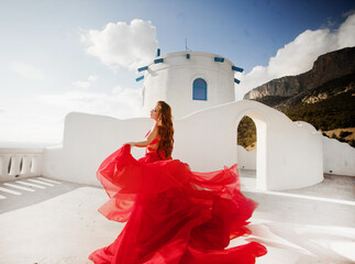 Fashion outdoor photo of gorgeous young woman with red hair in airy red dress posing on the streets...