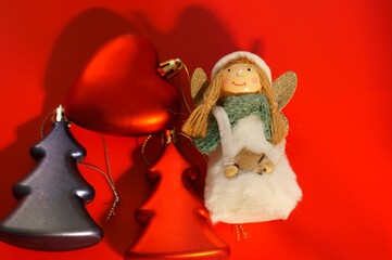 A red toy Christmas tree and an angel with a heart on a red background.