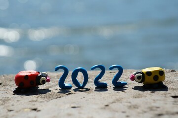 Obraz premium Figures of two ladybugs on a blue background. Between them is the number 2022.