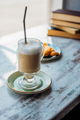 Latte in a tall glass against the background of a stack of books. The drink is on the table in a cafe.