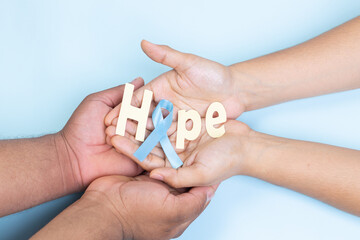 two hands holding word hope and light blue ribbon, prostate cancer, light blue background
