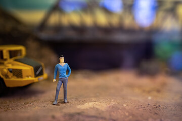 Toy model of male foreman worker standing in front of truck in the construction site.