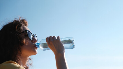 Girl with glasses drinks water from a bottle in hot weather. Space for text
