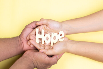 two hands holding word hope, childhood cancer, yellow background