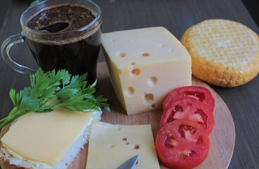 Cheese and tomatoes are on a wooden stand and a cup of coffee is on the table.	