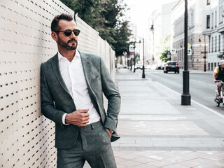 Portrait of handsome confident stylish hipster lambersexual model.Modern man dressed in elegant suit. Fashion male posing in the street background in Europe city at sunset. In sunglasses