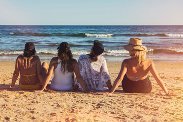 Group Of 4 Unrecognizable Women Sitting On The Beach Sand Looking At The Sea. Stock Photo Of Rear View Of 40 Year Old Women Enjoying A Sunny Day. Vacation Concept