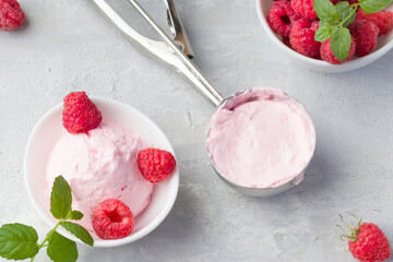 Fresh raspberries with mint and homemade ice cream in a white cup on a light background. Stainless steel spoon for ice cream balls. Delicious and romantic dessert. Top view