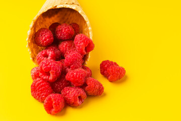 Summer, freshness and vegetarianism concept. Delicious and juicy raspberries in a waffle cone for ice cream on a yellow background. Copy space