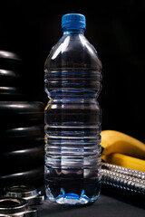 Dumbbell, sports equipment, water bottle, banana on a black background. Close-up