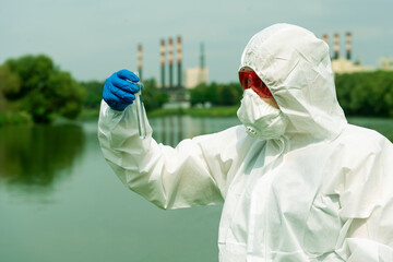 Sampling from open water. A scientist or biologist takes a water sample near an industrial plant....