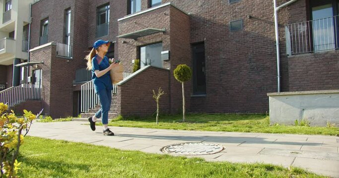 Delivery girl in uniform using smartphone app to find client address. Young caucasian woman courier with paper bag with goods looking for delivery place. Service and profession concept