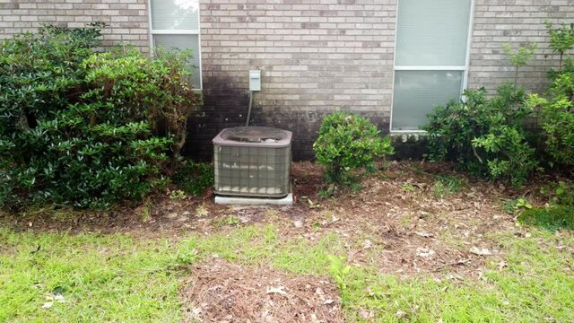 Old rusted Home air conditioner Unit next to brick home.