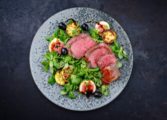 Modern style traditional fried dry aged angus beef filet medaillons with vegetable and lambs lettuce served as top view on a Nordic design plate
