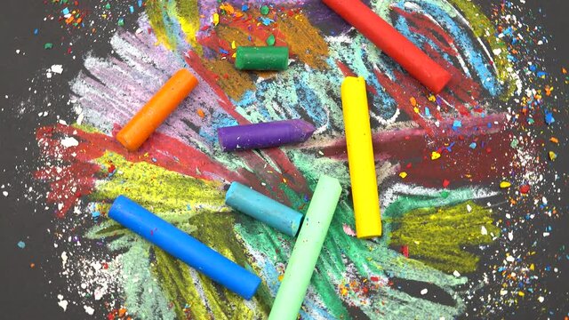 Multicolored wax crayons lie on the abstract background drawn by them. Black sheet of paper painted with wax crayons and wax crayons lying on it