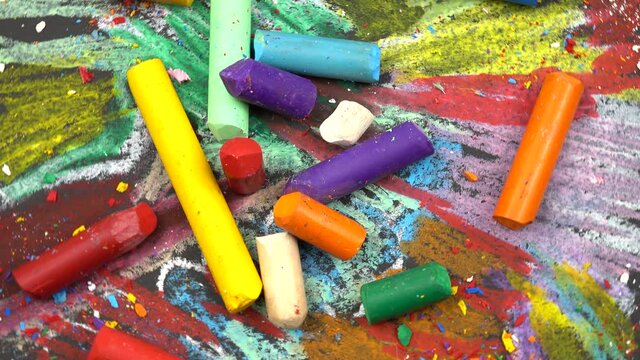 Multicolored wax crayons lie on the abstract background drawn by them. Black sheet of paper painted with wax crayons and wax crayons lying on it
