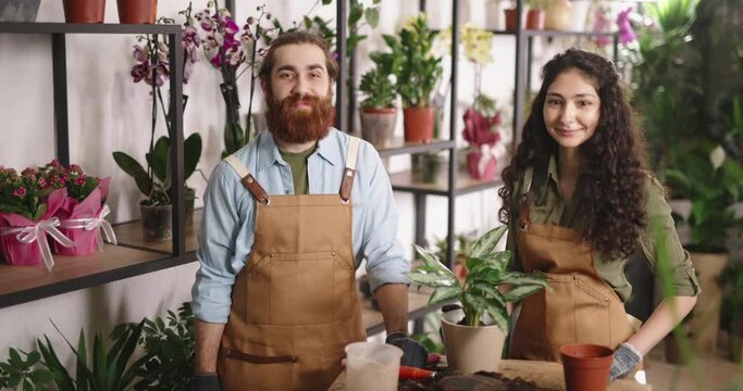 Portrait of two millennial florists working at flower shop. Greenhouse workers positively smiling and looking at camera - small business people 4k footage