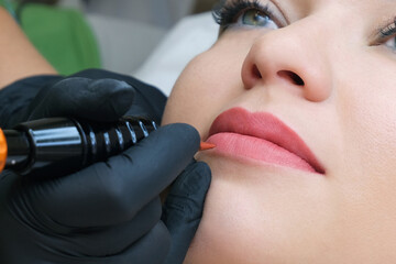 Young woman having permanent makeup on her lips at the beauticians salon. - obrazy, fototapety, plakaty