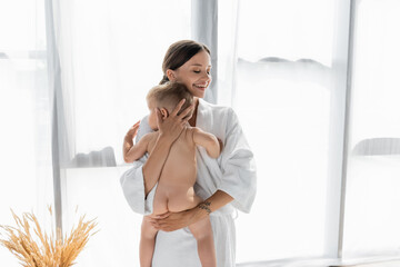 smiling mother in bathrobe holding in arms naked toddler son