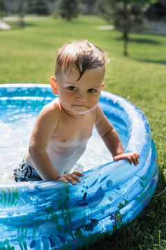 toddler boy standing in inflatable pool and looking at camera