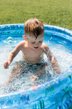 toddler boy sitting in inflatable pool and making water splashes
