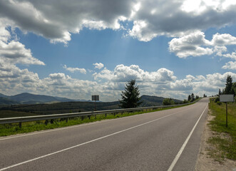 Asphalt road in mountain hilly countryside in pine forests, on background of blue sky with clouds, Ukraine, Carpathians