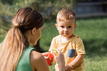 blurred mother holding bottle and bubble wand near toddler boy outside