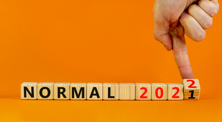 Symbol of covid-19 normal in 2022. Doctor turns wooden cubes and changes words 'normal 2021' to 'normal 2022'. Beautiful orange background, copy space. Medical, covid-19 normal in 2022 concept.