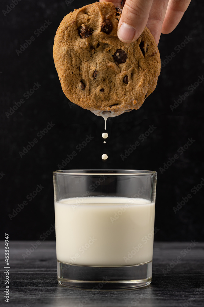 Wall mural Hand dipping chocolate chip cookie in glass of milk against dark background