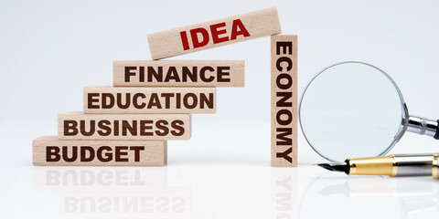 Magnifier, pen and wooden blocks with the text - Business, Budget, Education, Economics, Finance and IDEA