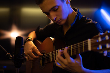 Fototapeta premium Man with a classical guitar in a neon glow. Teenager plays guitar. Young man plays a musical instrument.