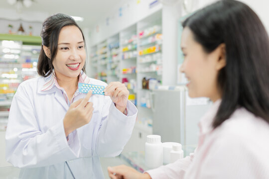 asian female pharmacist explain about how to use contraceptive drug, she holding contraceptive drug strip pack with her hand and talk with customer in drugstore, Oral contraceptive pill